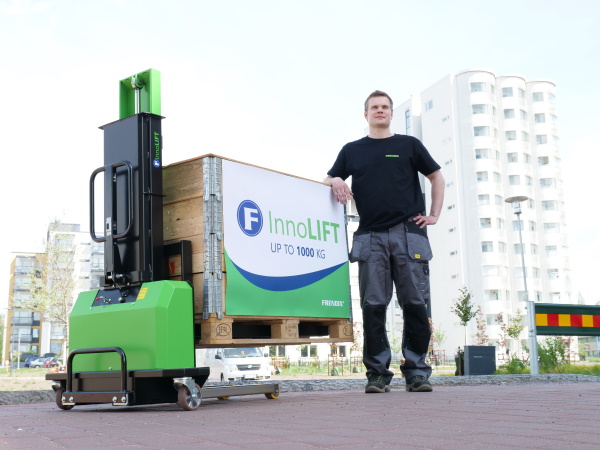 A man standing behind an InnoLIFT machine and it's cargo and in front of a white apartment building.