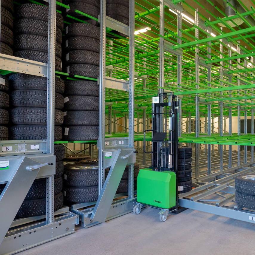 A tire warehouse with empty and filled racks and a tire stacker pushed against the racks.