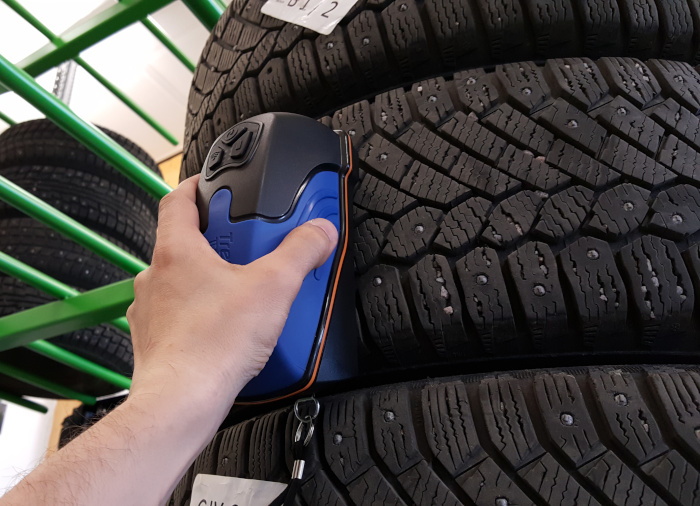 A hand using a tire depth scanner on a tire placed on tire rack.