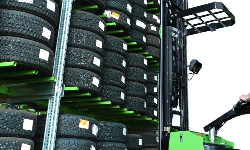 A tire rack filled with tires and a tire stacker with an overhead guard.