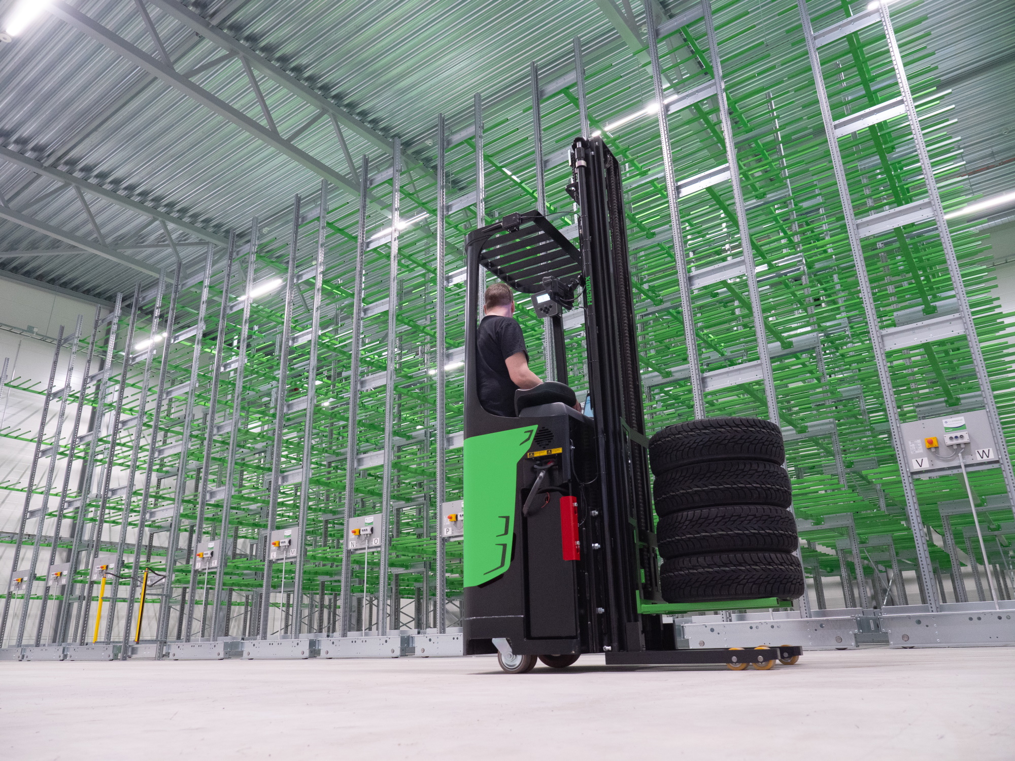 A man driving a tire stacker in a tire warehouse with empty racks.