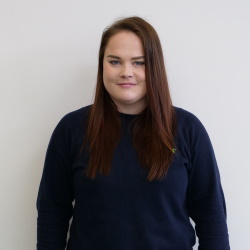 A young woman with long brown hair in a deep blue shirt from the chest up.